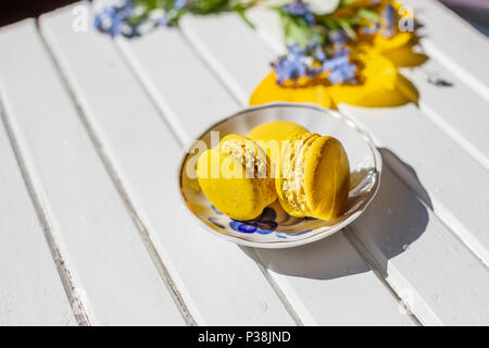 Yellow tasty macaroni cookies on the plate. Candy bar. Children's birthday.French dessert on white wooden background. Flowers, macarons in lemon color .Copy space Stock Photo