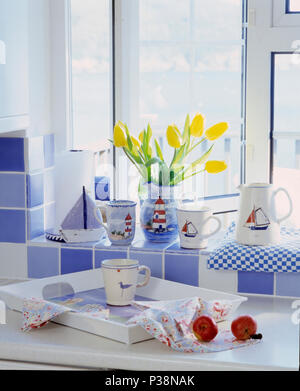 Close-up of collection of coastal crockery on blue+white tiled windowsill above white tray on kitchen worktop Stock Photo