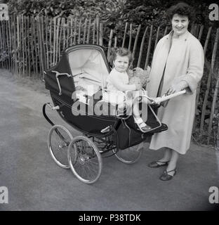 1950s, historical picture of a mother outside with her baby and her little girl sitting on top of their Royale coach-built pram holding her teddy bear, England, UK. The Royale was a luxury coach built pram made by the 'Royal Baby Carriage Co' of Nunhead Grove, London, founded by brothers Alf & Frank Saward, who claimed to make the 'world's most beautiful prams'. Stock Photo