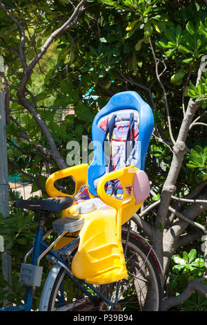 Colourful plastic child's safety seat attached to a bicycle  for transportation of a baby or toddler. parked in front of shrubs. Close up view. Stock Photo