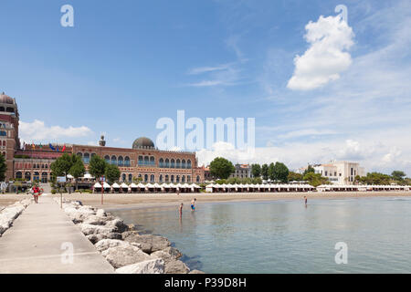 View from the breakwater of the seashore, beach,  Hotel Excelsior and Casino, Lido di Venezia, Venice, Veneto, Italy with people bathing and cabanas Stock Photo