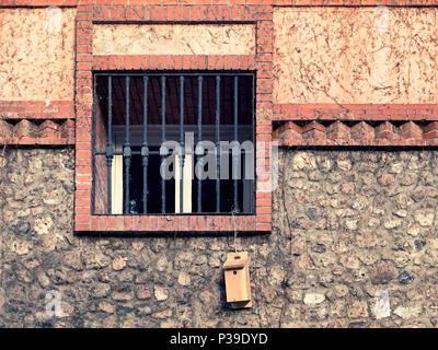 window with iron grating on a rustic facade and a small wooden house hanging Stock Photo