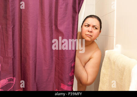 A woman looks out cautiously from behind her shower curtain, concerned she heard a noise Stock Photo
