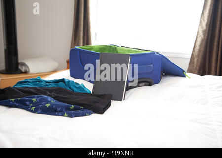 Pajamas and book on a bed beside a suitcase ready to travel Stock Photo
