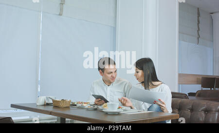 Two colleagues discussing work while eating lunch in a cafe Stock Photo