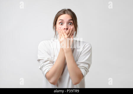 attractive, pretty,and charming, woman closed her mouth with crossed hands and wide opened eyes, looking at camera. She can't believe her eyes Stock Photo