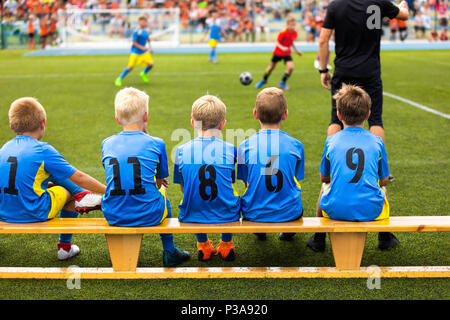 Football soccer game for children. Kids substitute players sitting on a bench. Football sports tournament for young boys Stock Photo