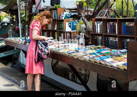 Girl looking at books at Word on the Water floating bookshop on a barge, Regent's Canal near Kings Cross, London, UK Stock Photo