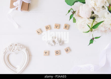 Top view Love you lettering with statuette of two little antique lovely angels, vintage heart shaped photo frame, giftbox and white peonies bouquet on Stock Photo