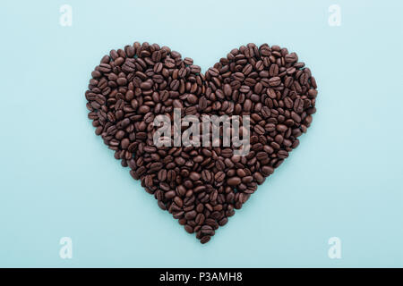 Perfect heart shape made of coffee beans on blue background. Flat lay, minimal design. Symbol of Love to coffee. Stock Photo