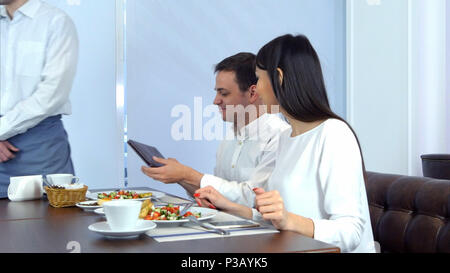Happy young couple paying bill brought by waiter and leaving cafe Stock Photo