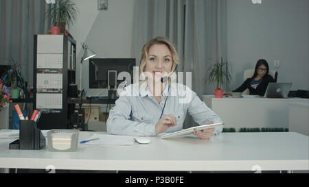 Smiling call center agent using tablet and talking to the camera Stock Photo