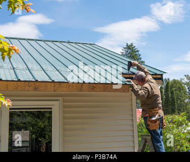 Construction worker on a ladder repairing damage to a green metal roof in Speculator, NY USA Stock Photo