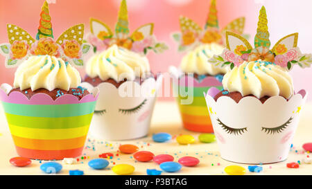 Adelaide, South Adelaide - June 15, 2018: Decorating children's birthday party unicorn and rainbow themed cupcakes, close up against a colorful pastel Stock Photo