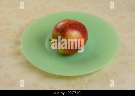One freshly rinsed Gala apple on green plate on tablecloth Stock Photo