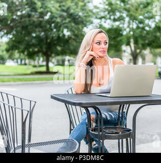 Woman sitting at a bistro table outside looking to the side with a laptopo opened. Stock Photo