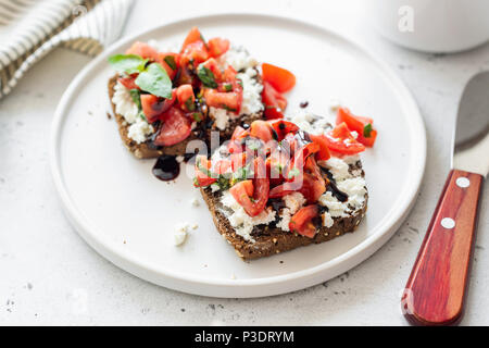 Bruschetta with tomato, cheese and balsamic sauce on white plate. Whole grain toast with cheese and tomatoes. Healthy breakfast or snack
