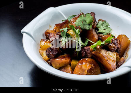 Chinese beef stew with young potatoes in sweet sauce, in white plate on black background Stock Photo