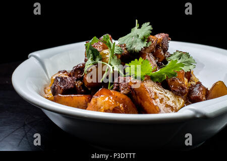 Chinese beef stew with young potatoes in sweet sauce, in white plate on black background Stock Photo