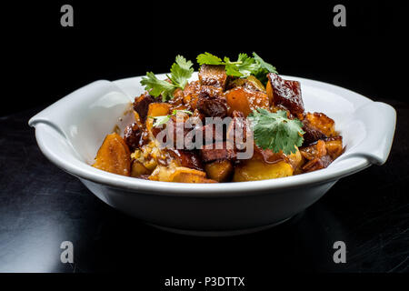 Chinese beef stew with young potatoes in sweet sauce, in white plate on black background Stock Photo