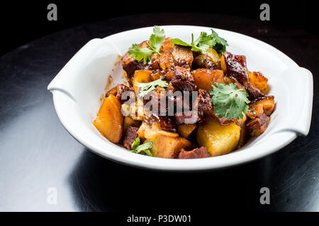 Chinese beef stew with young potatoes in sweet sauce, in white plate on black background Stock Photo