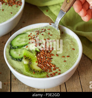 In a plate with green smoothies with flax seeds, a female hand dropped a spoon on wooden background Stock Photo