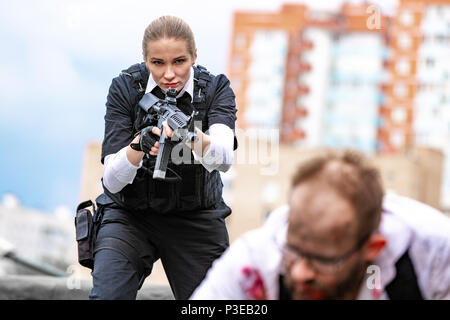 Woman soldier, spy agent killer or police woman with a gun in her hand holding at gunpoint a man lying on the ground Stock Photo