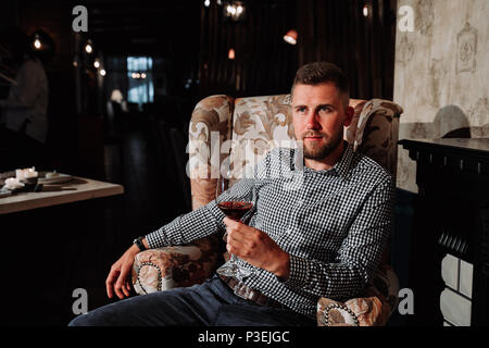 a young man sitting on a chair in an expensive restaurant and drinking wine Stock Photo