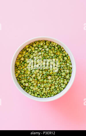 Raw uncooked green peas in a white bowl on a  pink background. Top view. Stock Photo
