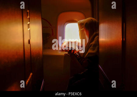 A man is putting on a tefillin and praying at sunrise inside of an airplane over the ocean Stock Photo