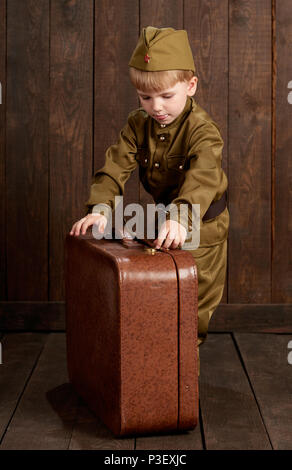 children boy are dressed as soldier in retro military uniforms with old suitcase, dark wood background, retro style Stock Photo