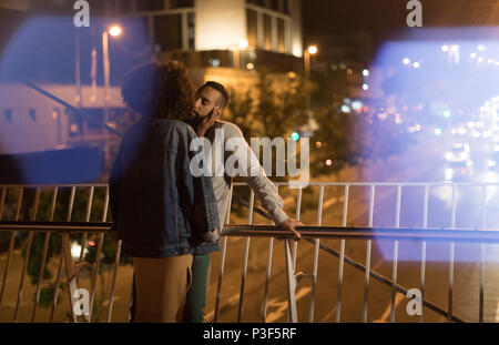 Couple kissing each other while standing near railing Stock Photo