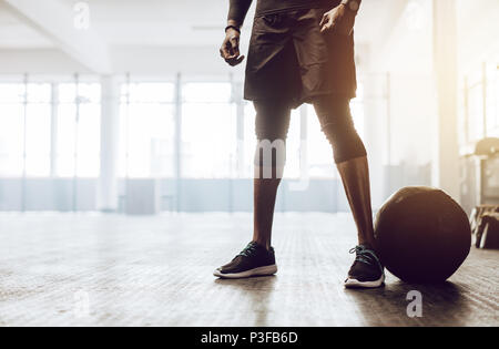 Athletic man standing in the gym beside a medicine ball. Close up of the lower half of a man working out in gym. Stock Photo