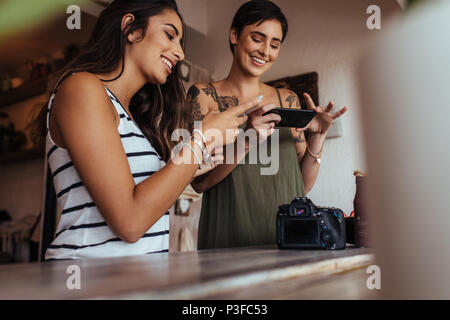 Women bloggers shooting photos of smoothie jar placed beside a DSLR camera for an article on food blog. Food bloggers taking photos for their food blo Stock Photo