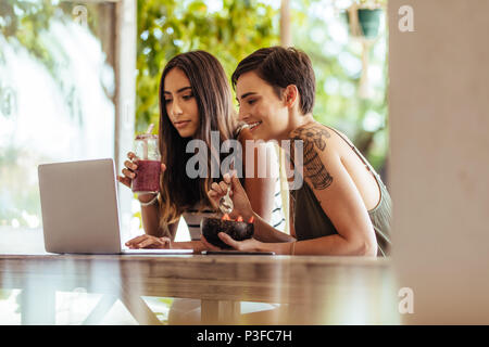 Two women sitting at a restaurant working on a laptop computer. Women sitting at a restaurant enjoying smoothie and a dessert. Stock Photo