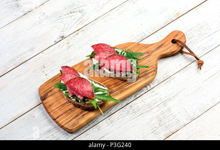Tasty appetizer of thinly sliced spicy salami on bread with cheese and herbs on a cutting board with copy space Stock Photo