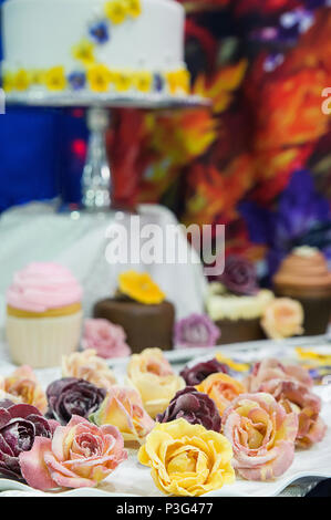 Wedding cake and cupcakes decorated with edible flowers with focus on the cake with focus on the edible crystallized flowers Stock Photo