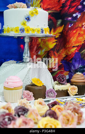 Wedding cake and cupcakes decorated with edible crystallized flowers with focus on the cake Stock Photo