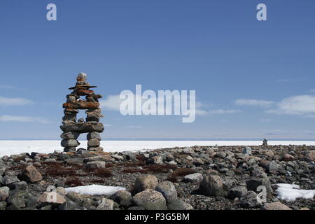 Inukshuk or Inuksuk landmark with frozen bay in the background near Arviat, Nunavut Stock Photo