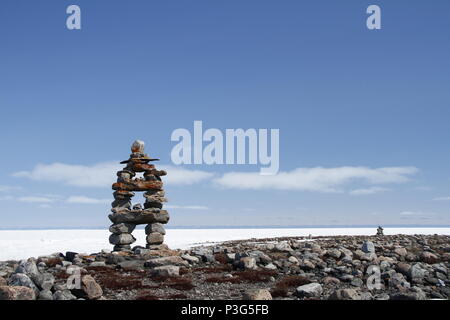 Inukshuk or Inuksuk landmark with frozen bay in the background near Arviat, Nunavut Stock Photo