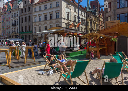 Locals and tourists relax on deckchairs in the sun on makeshift beach in the Market Square, Wrocław, Poland Stock Photo