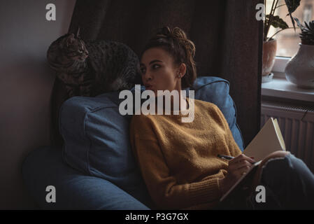 Woman pouting at her pet cat while writing in the diary Stock Photo