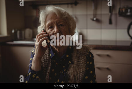 Worried senior woman talking on the phone in the kitchen Stock Photo