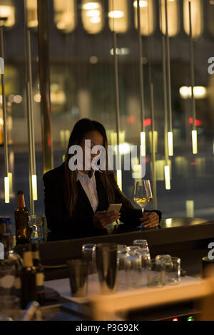 Businesswoman standing at bar having champagne while using her phone Stock Photo