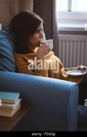 Young woman relaxing on sofa having a coffee during daytime at home Stock Photo