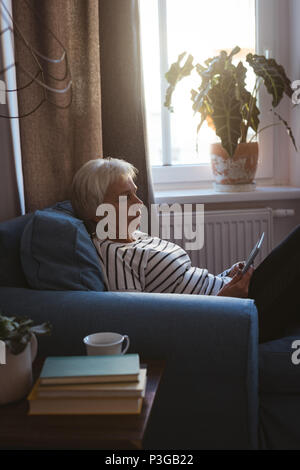 Senior woman sitting on sofa using her tablet in living room Stock Photo