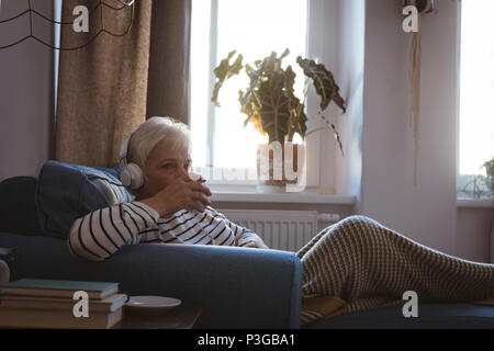 Senior woman relaxing on sofa listening to music with a cup of coffee in living room Stock Photo