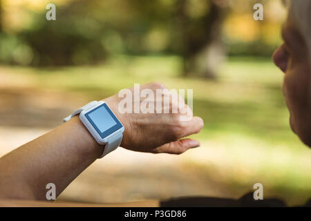 Senior woman using a smart watch in a park on a sunny day Stock Photo