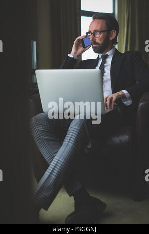 Businessman talking on mobile phone while using laptop Stock Photo