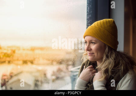 Woman wearing yellow beanie looking outside window Stock Photo